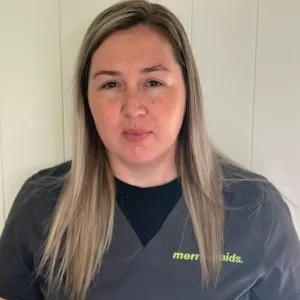smiling woman with a grey merry maids uniform standing in front of a tan wall